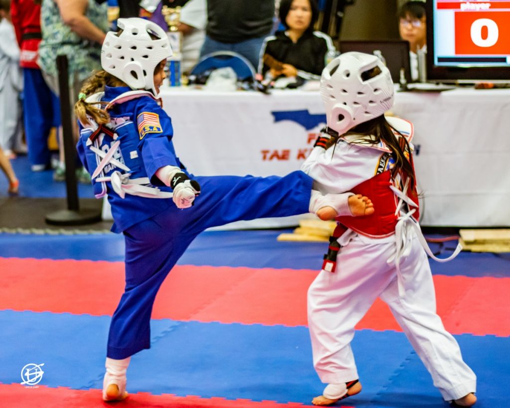 two uniformed young girls sparring in tae kwon do tournament