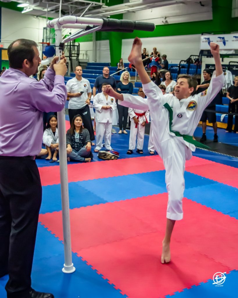 Young male competitor in tae kwon do tournament performing a high kick