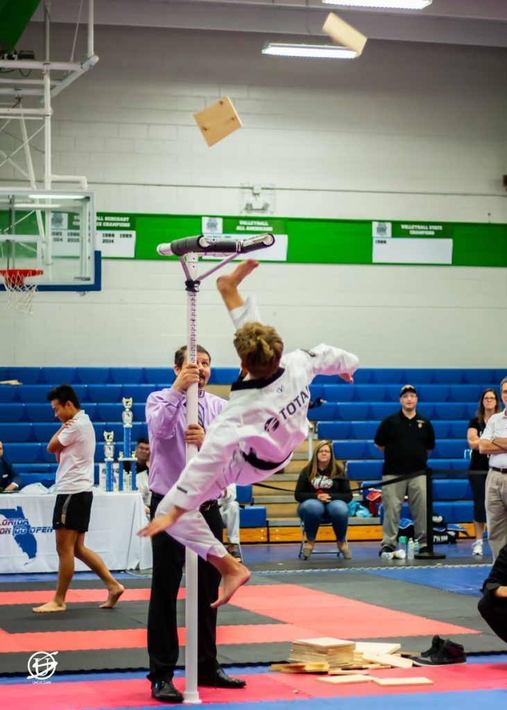 Young male competitor in tae kwon do tournament performing kicking a board off a high stand