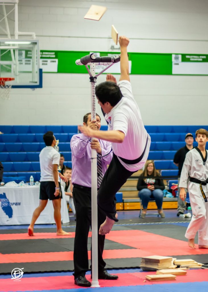 Young male competitor in tae kwon do tournament performing kicking a board off a high stand